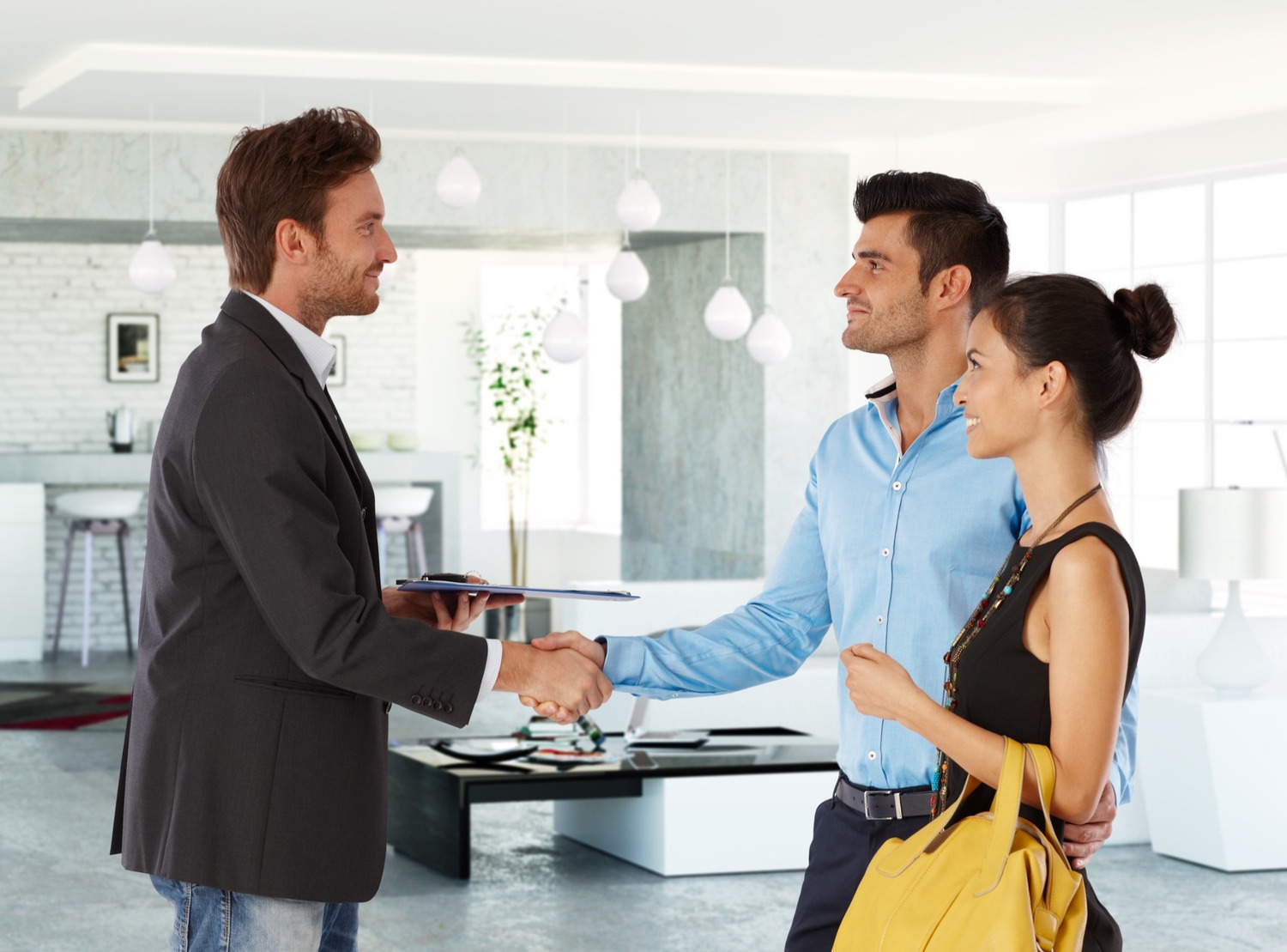 asesor inmobiliario estrecha mano de cliente junto a su joven esposa